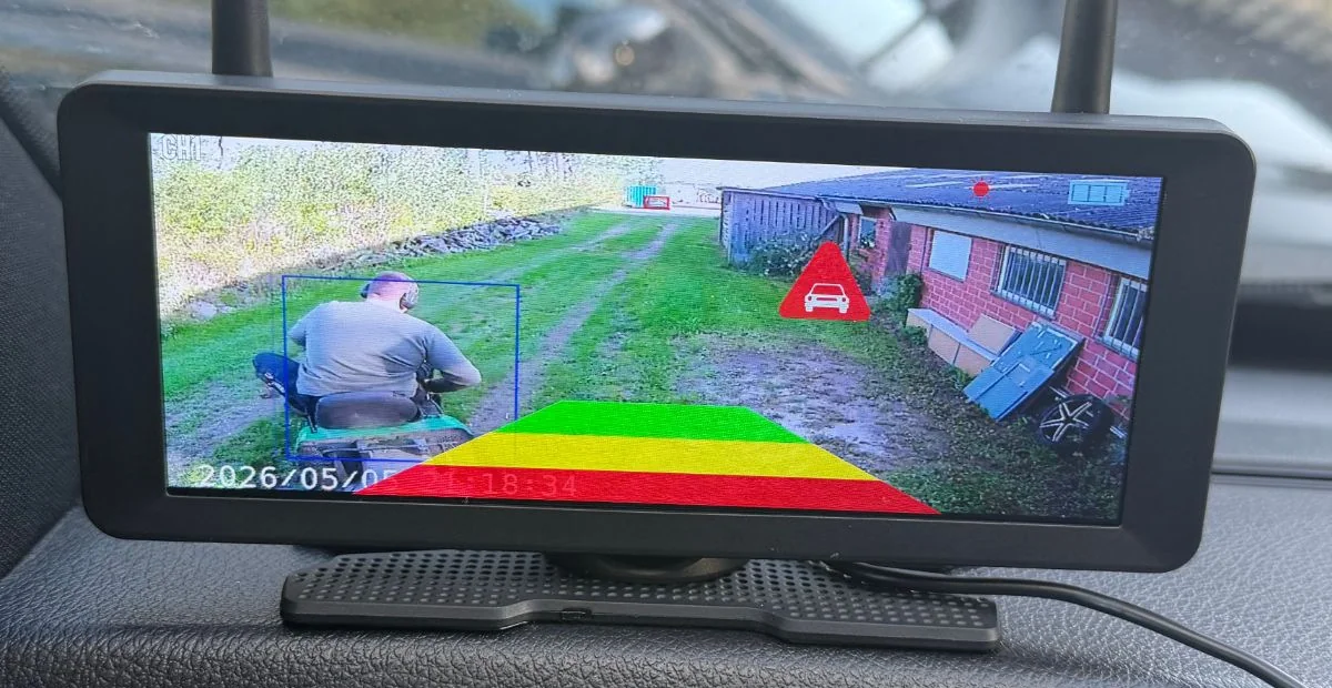 Warndreieck mit Fahrzeug-Symbol, blauer Rahmen um die Person auf dem Aufsitzmäher und farbige Warnzonen. Datum und Uhrzeit im Monitor waren noch nicht eingestellt