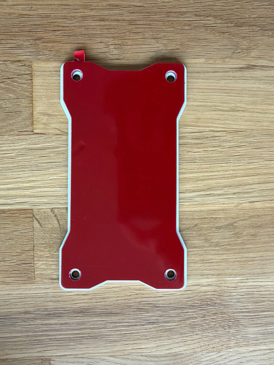 Die Montageplatte mit roter Schutzfolie über der Klebefläche und vier Schraublöchern